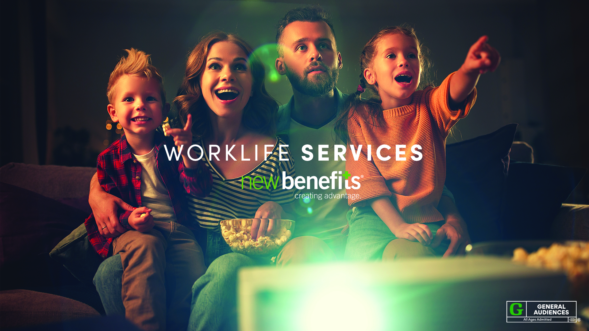 Mother, father, daughter, and son sitting close together on sofa behind projector in dark living room, eating popcorn, smiling, looking forward, Worklife Services, New Benefits logo, and "G" General Audiences rating superimposed